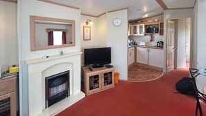 A living room with a fireplace, television, and kitchen area with cabinets and a microwave. - 2 bedroom accommodation in Burnham-on-Sea (Burnham-on-Sea)