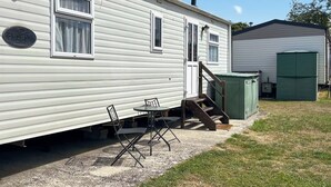 A mobile home with a patio area, a table, chairs, and a green utility shed. - 2 bedroom accommodation in Burnham-on-Sea (Burnham-on-Sea)