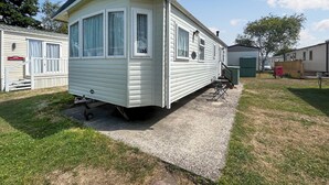 A mobile home with a porch, a small patio, and a grassy yard. - 2 bedroom accommodation in Burnham-on-Sea (Burnham-on-Sea)