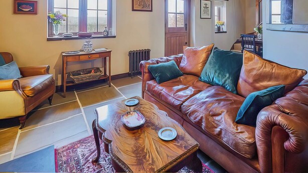 A living room with a leather sofa, wooden coffee table, and a window with curtains. - 2 bedroom accommodation in Llangadog (Llangadog)