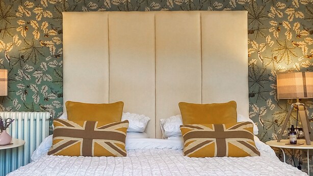 Un lit recouvert d’une couette blanche matelassée, deux oreillers ornés du motif Union Jack et une tête de lit avec des panneaux verticaux.