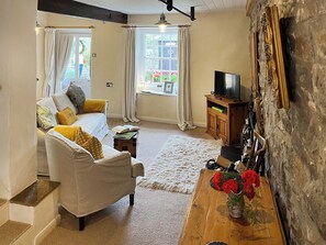 A living room with a sofa, a coffee table, a television on a wooden cabinet, and a stone wall. - Lock Heather Cottage (Healaugh, near Reeth)