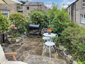 A stone patio with a grill and white metal chairs.