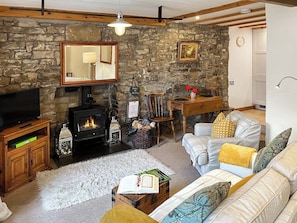 A cozy living room with a stone wall, a fireplace, a television, and a comfortable sofa. - Lock Heather Cottage (Healaugh, near Reeth)