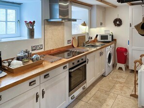 A kitchen with a stove, microwave, sink, and a washing machine. - Lock Heather Cottage (Healaugh, near Reeth)