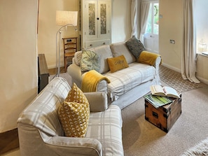 A living room with a sofa, a side table, a lamp, a cabinet, and a window with curtains.