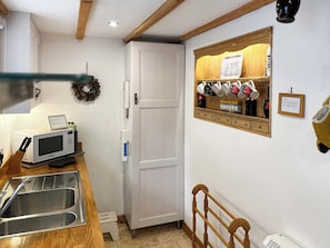 A kitchen with a microwave, sink, and a wooden cabinet with mugs and bottles. - Lock Heather Cottage (Healaugh, near Reeth)