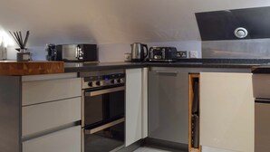 A compact kitchen with a built-in oven, a coffee maker, and a kettle on the countertop.