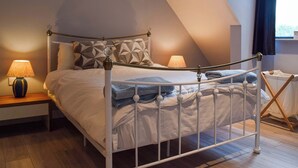 A bedroom with a sloped ceiling, a metal bed frame, patterned pillows, bedside lamps, and a view of the outdoors.