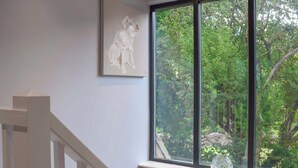A room with a large window, a painting on the wall, and a vase on the windowsill.