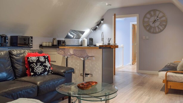 A modern living room with a glass coffee table, leather sofa, and a kitchen area with a microwave and kettle.