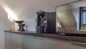 A modern kitchen with a coffee maker, a kettle, and a refrigerator.