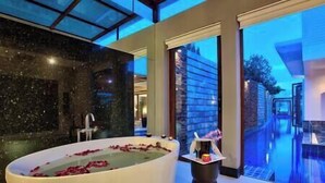 A modern bathroom with a large bathtub filled with rose petals, a black marble wall, and a view of a cityscape through large windows.