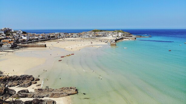 A coastal town with a sandy beach, clear blue waters, and a mix of residential and historical buildings.