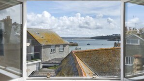 A view from a window overlooking a harbor with boats, a lighthouse, and a hilly landscape.