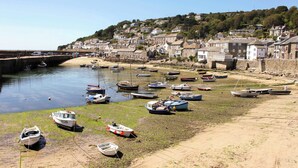 A coastal town with boats docked along the shore and houses on a hillside in the background.