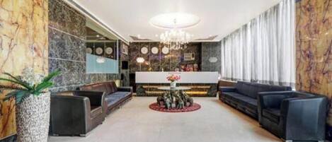A spacious lobby with a central seating area, a chandelier, and a reception desk.