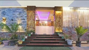 A hotel entrance with a stone facade, steps leading to a door, and potted plants.