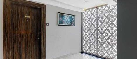 A hallway with a wooden door, a framed artwork on the wall, and a decorative panel with a floral pattern.