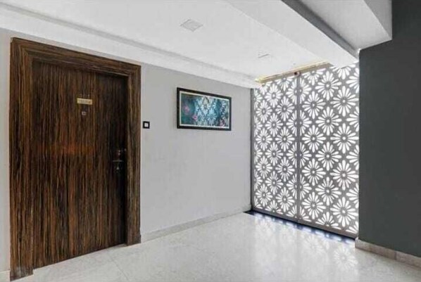 A hallway with a wooden door, a framed artwork on the wall, and a decorative panel with a floral pattern. - The Vishwanath Palace (Misrikh)