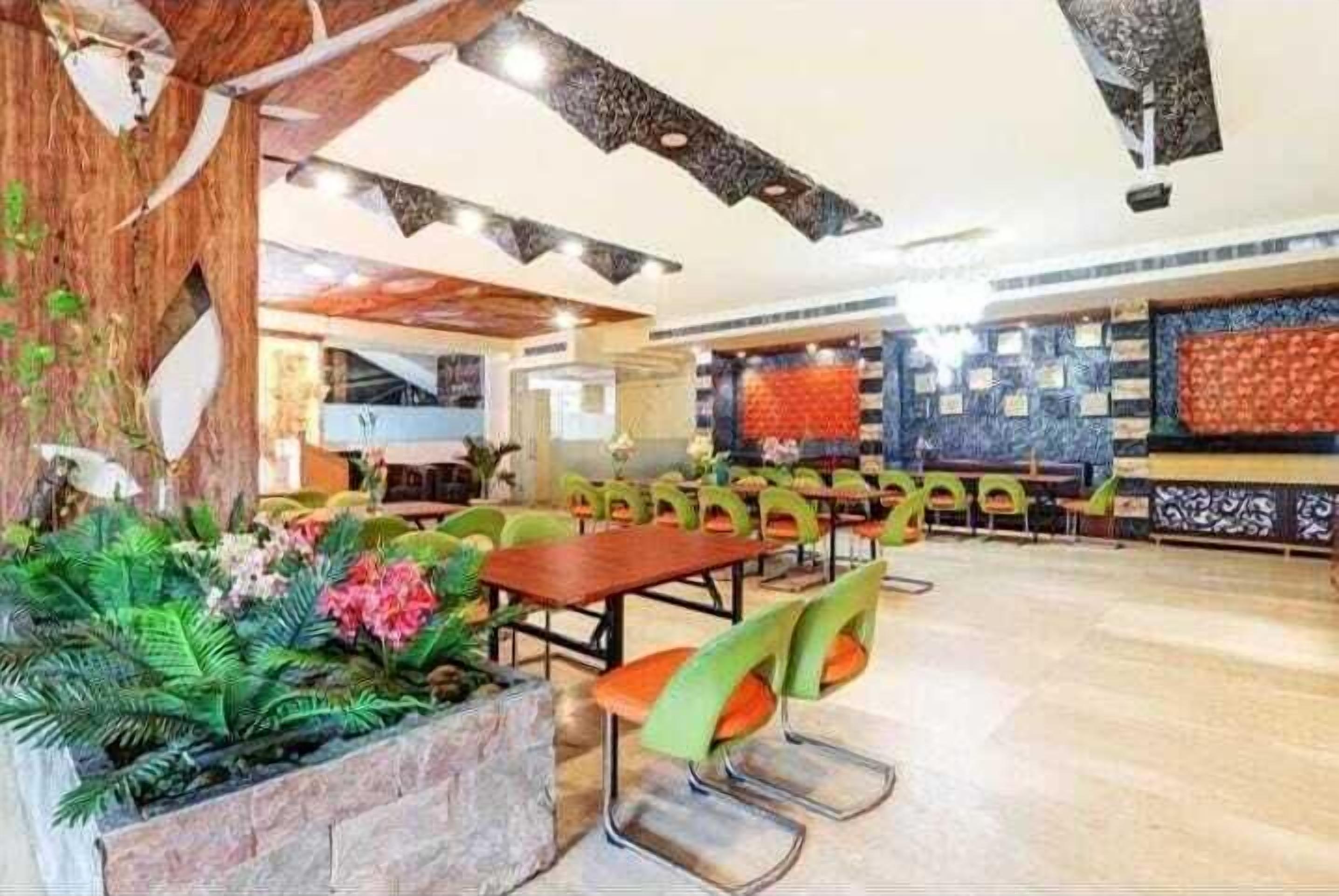 A spacious indoor area with multiple tables and chairs, a stone planter with greenery, and a patterned wall in the background.