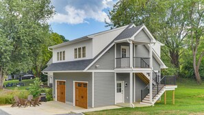 Ein zweistöckiges Haus mit Veranda, Garage und überdachter Sitzgelegenheit.
