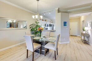 Un coin repas comprenant une table en verre, quatre chaises, un lustre et un miroir au mur.
