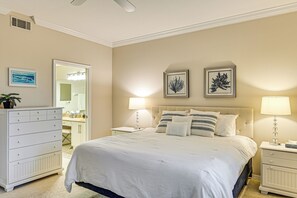 Une chambre à coucher avec un grand lit, deux tables de chevet avec des lampes, une commode et des œuvres d’art encadrées accrochées au mur.