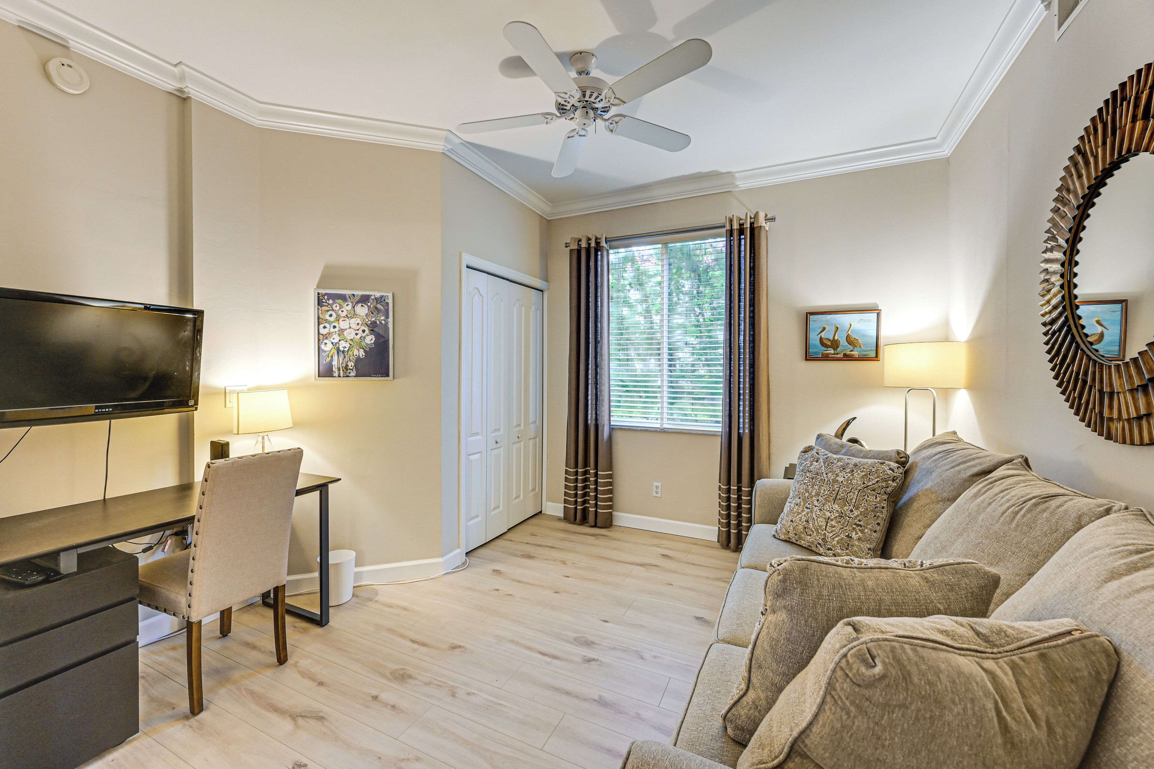 A living room with a TV, a ceiling fan, a sofa, and a dining area with a chair.