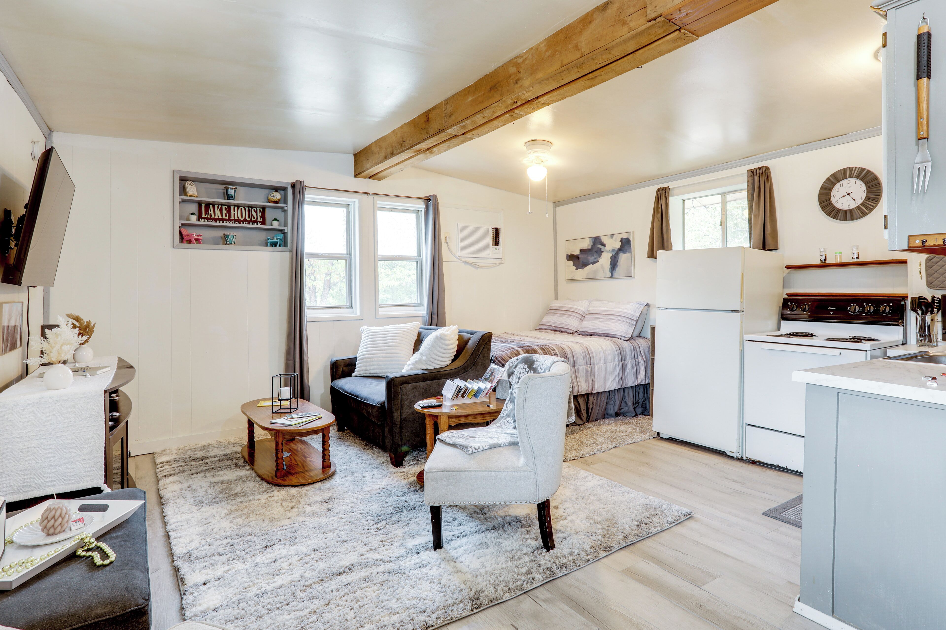 A cozy, well-lit room with a bed, a chair, a small table, and a kitchen area with a refrigerator and stove.