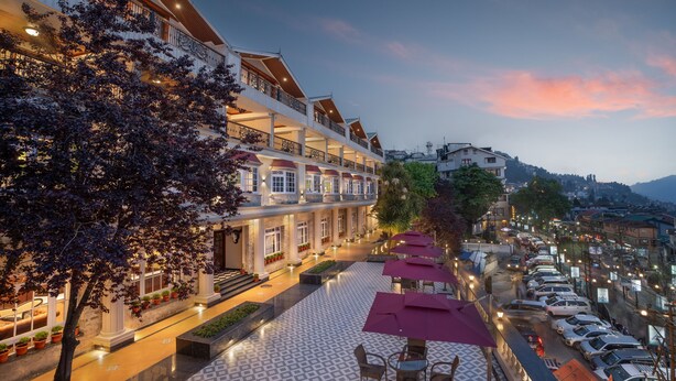 Un hotel con estructura de varios pisos, mesas al aire libre con sombrillas y vistas de la ciudad circundante.