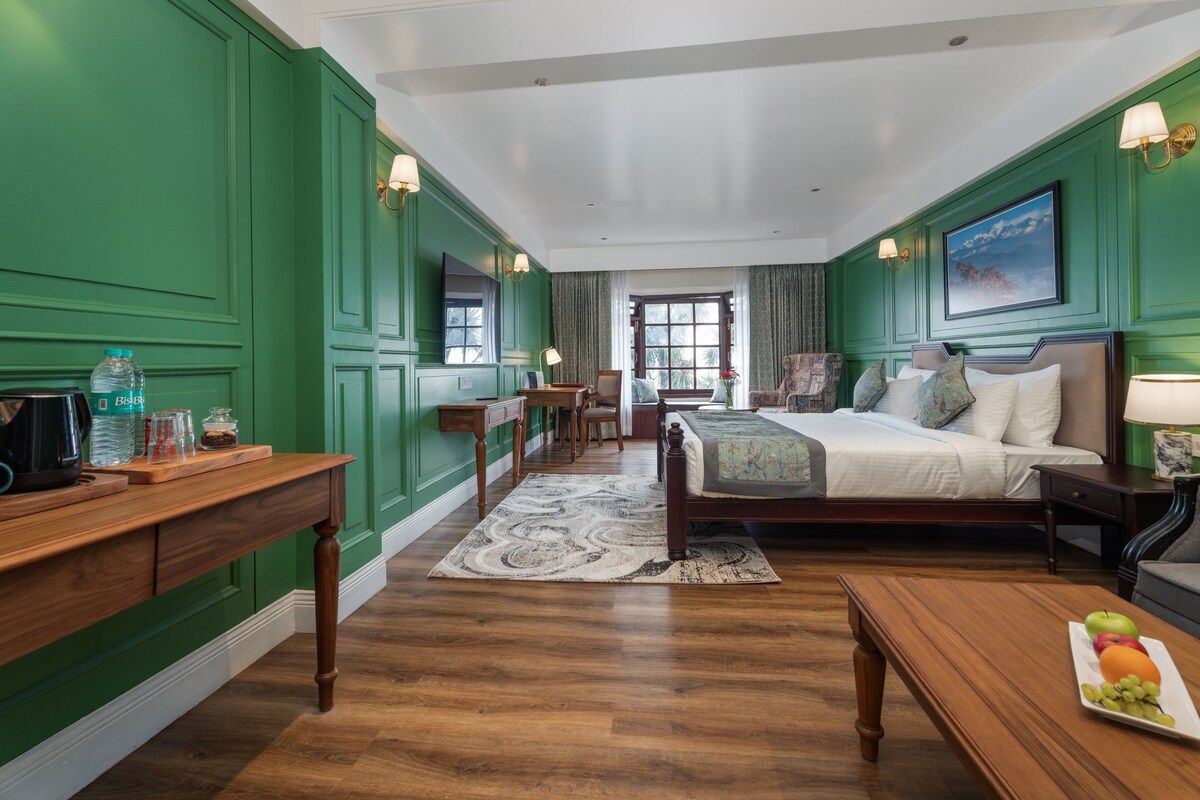 Habitación de hotel con paredes verdes, una cama de madera, un escritorio con cafetera y vistas al exterior a través de una ventana.