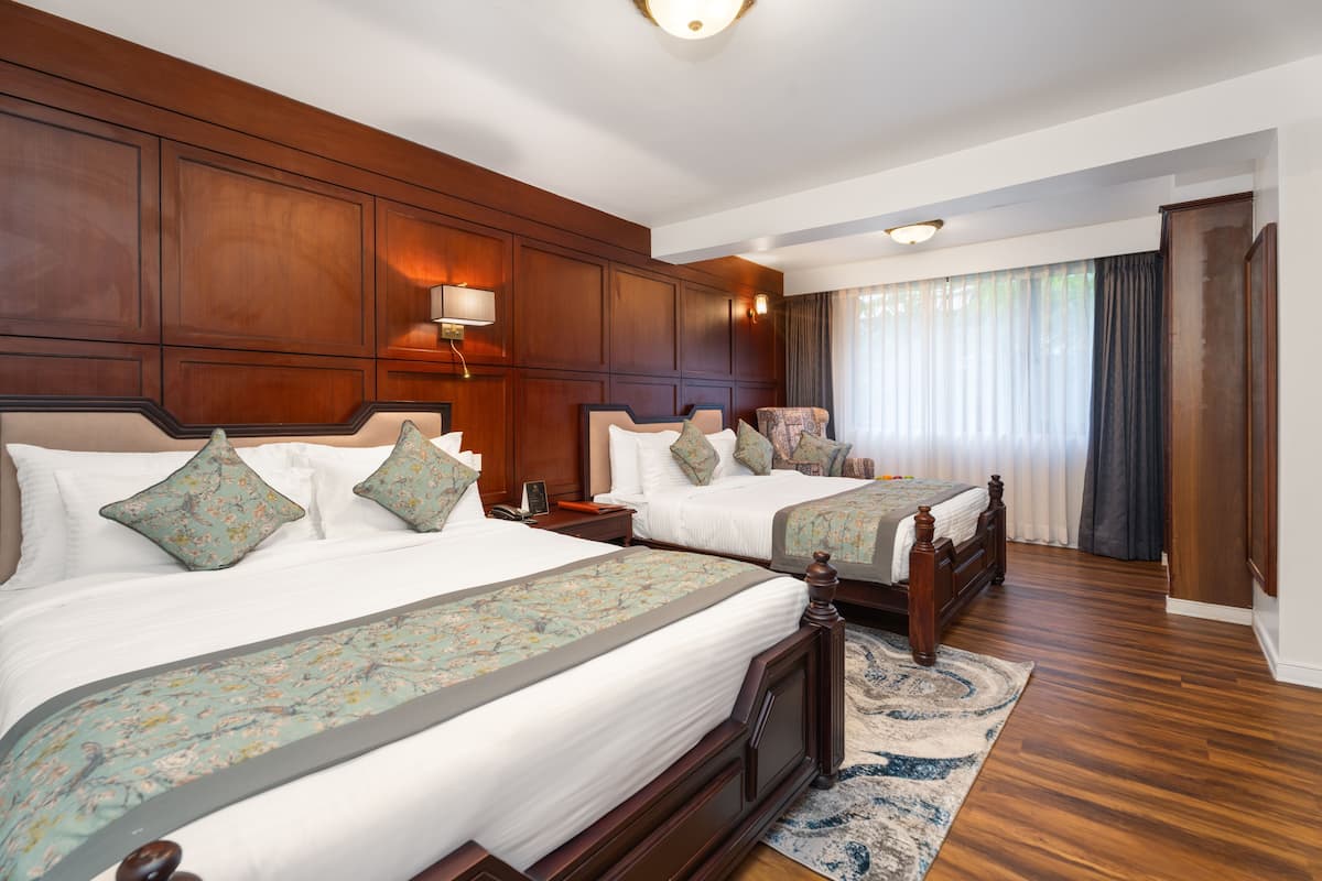 Een hotelkamer met twee houten bedden, een groot raam met gordijnen en een houten vloer.