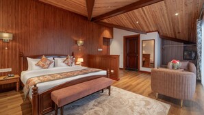 Un dormitorio con techo de madera, una cama grande con un banco, una mesita de noche, un aparador y una silla.