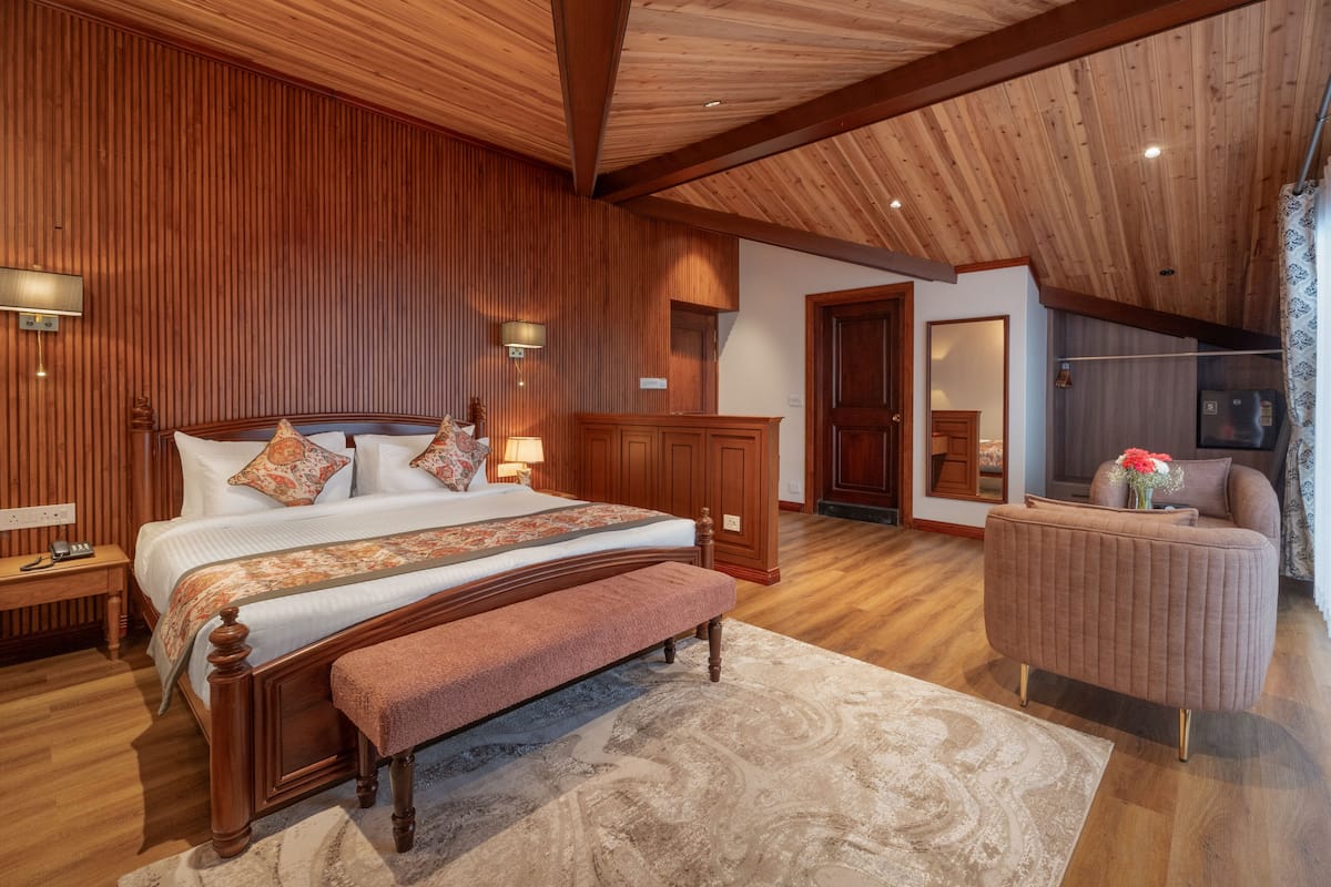 Een slaapkamer met een houten plafond, een groot bed met een bankje, een nachtkastje, een dressoir en een stoel.