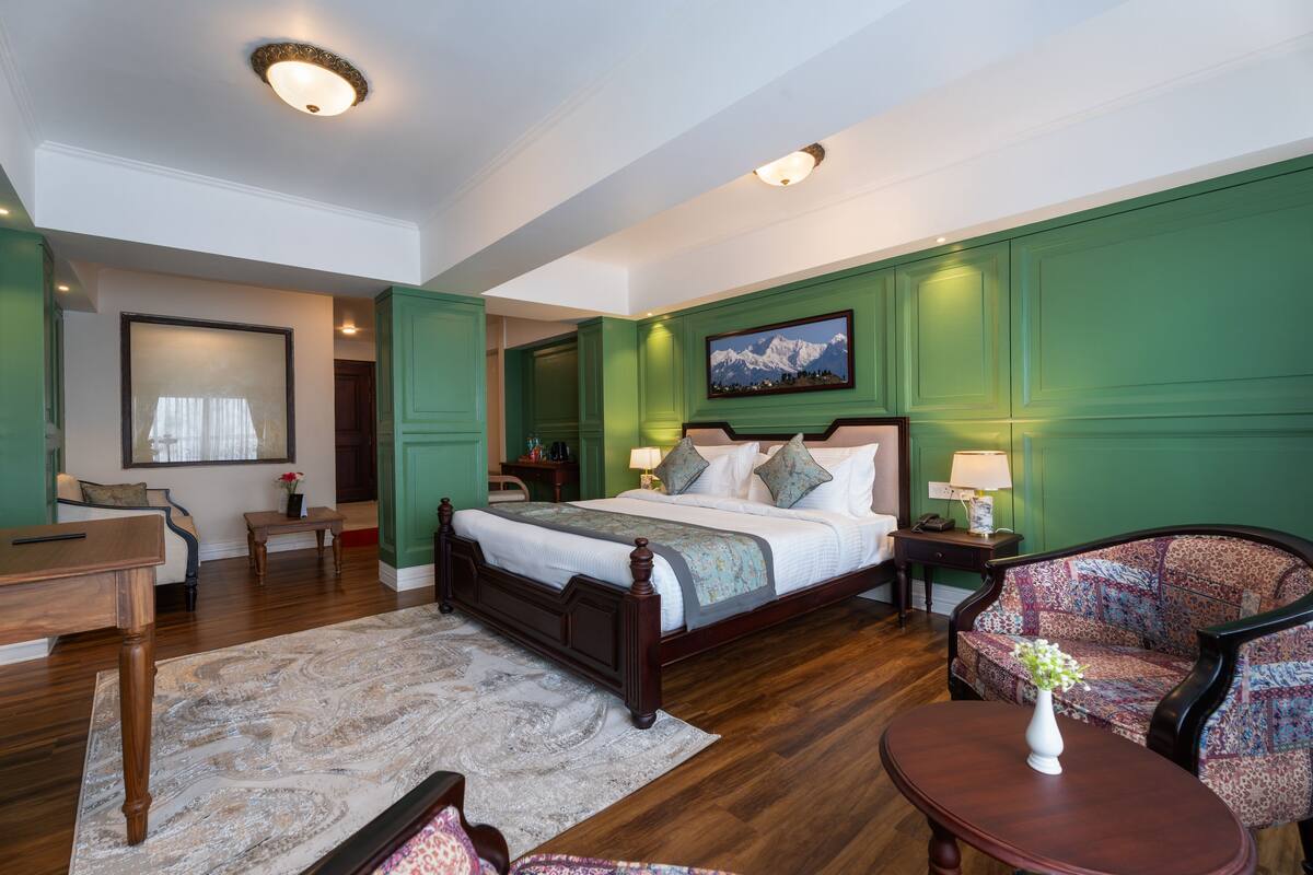 Een ruime slaapkamer met een groot bed, een zithoek met een bank en fauteuil, een houten salontafel en een schilderij aan de muur.