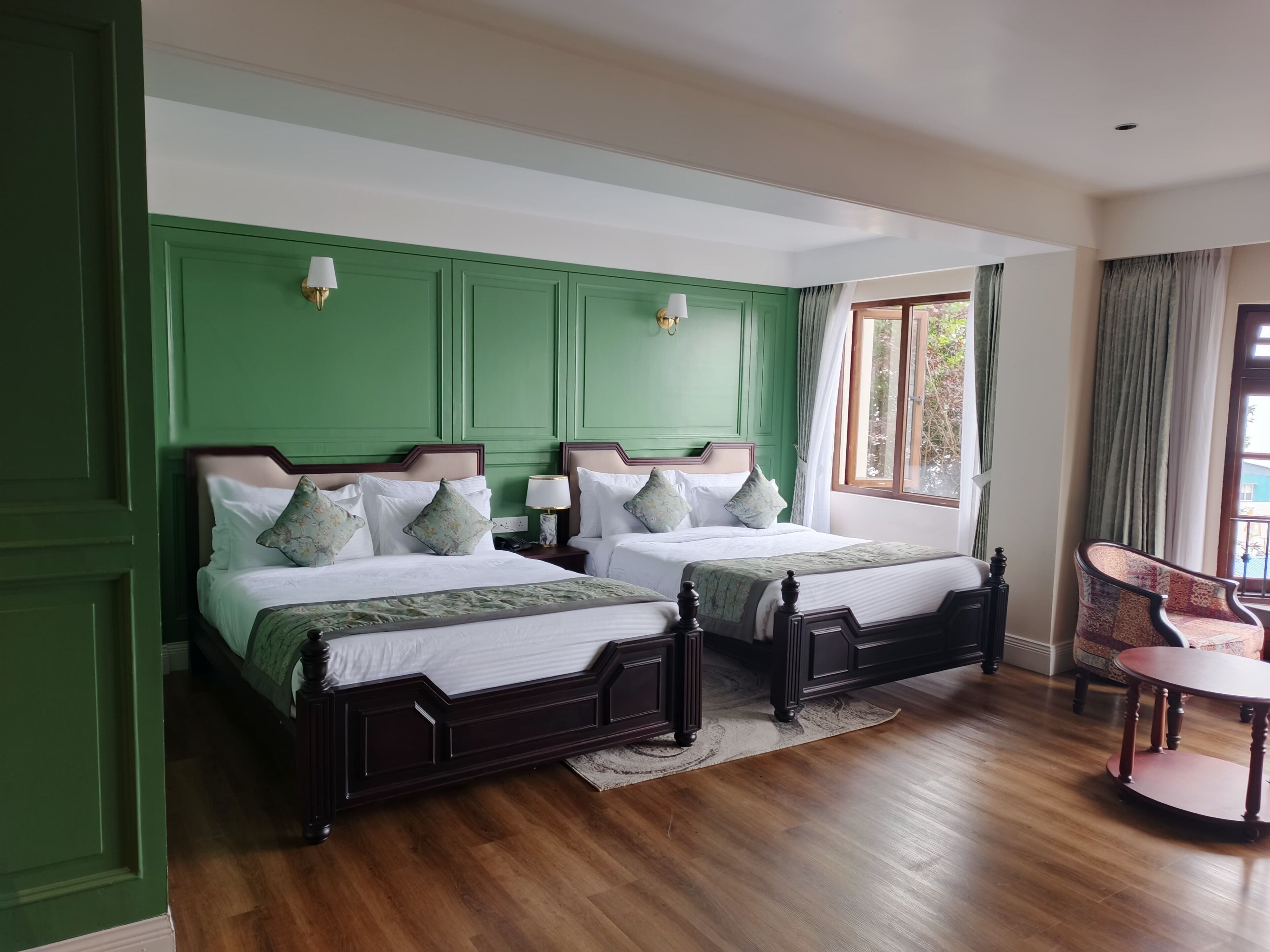 A hotel room with two beds, a small round table, and a view of the outdoors through a window.