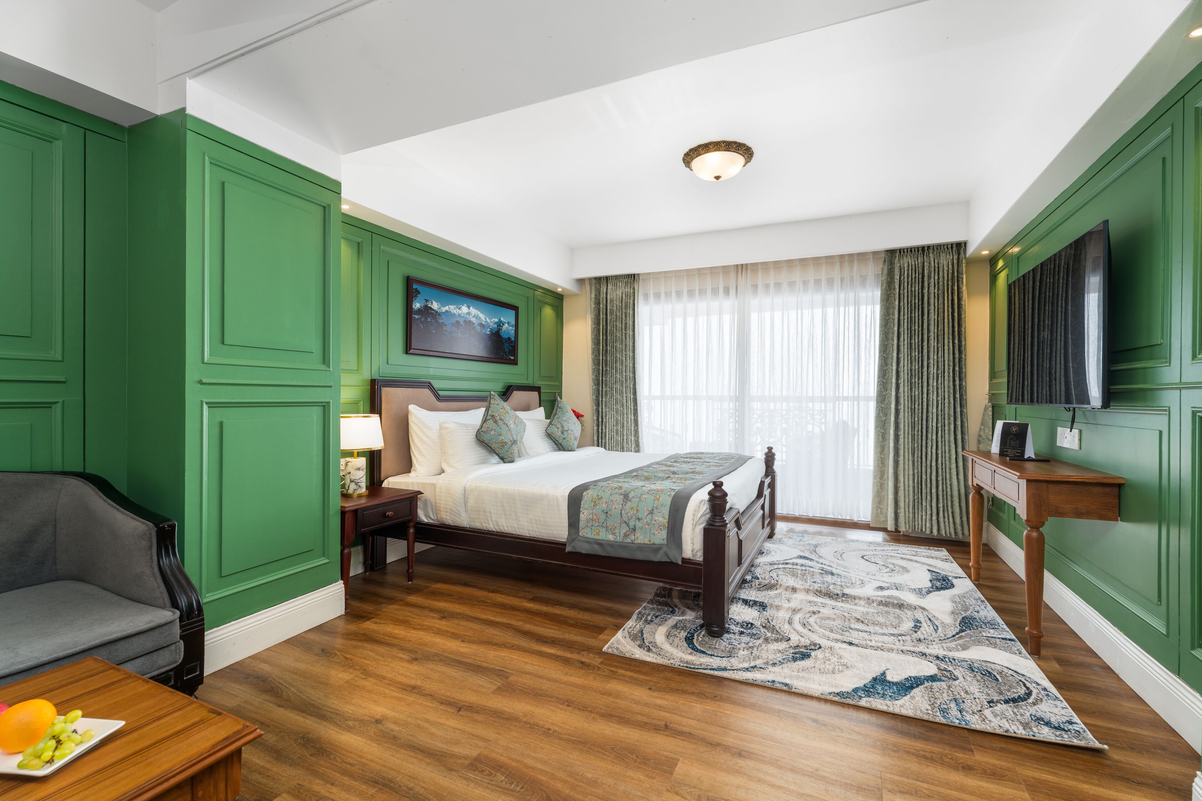 A bedroom with a bed, a nightstand, a lamp, a TV, a sofa, and a wooden floor.