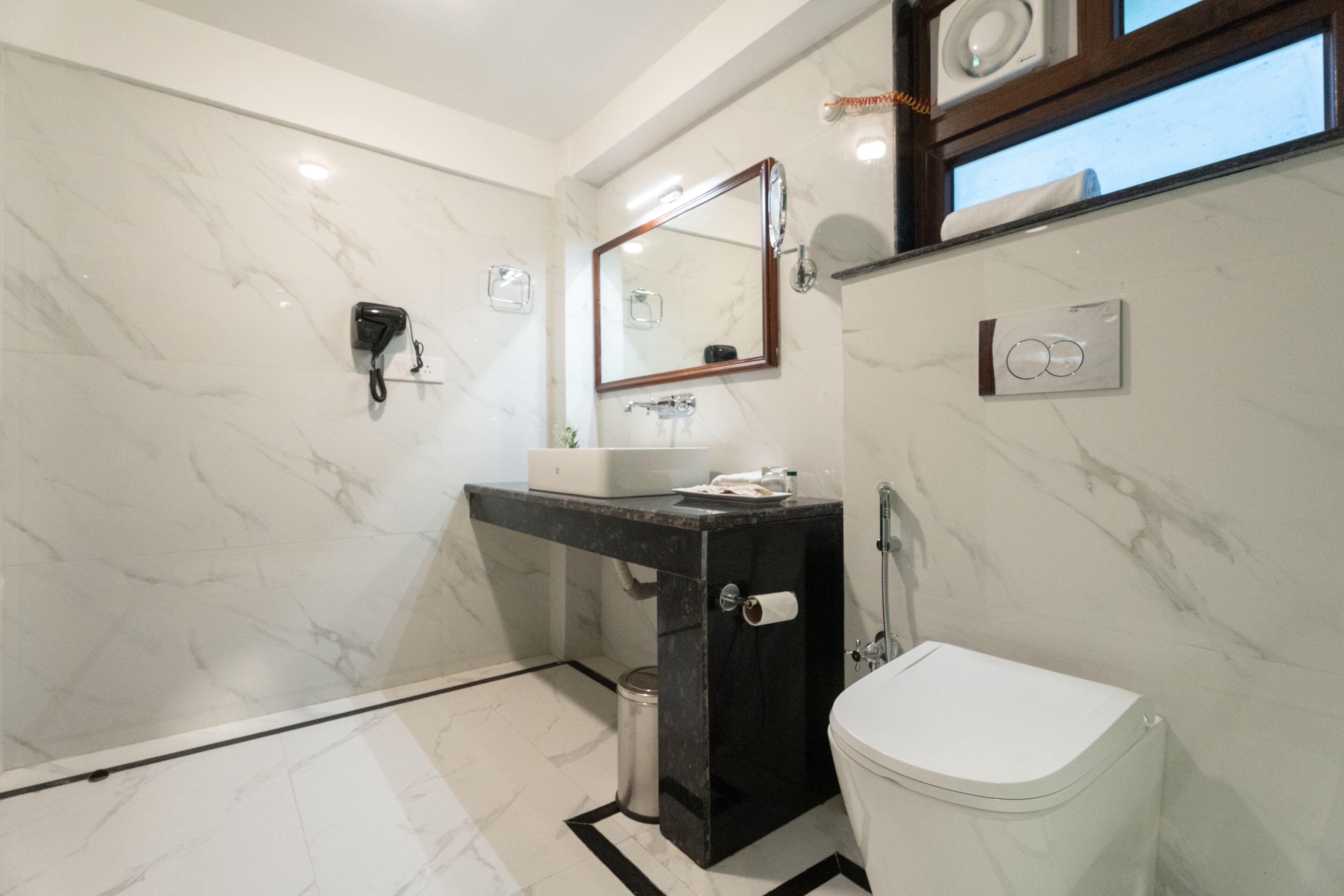 Une salle de bain moderne avec un sol en marbre, un lavabo noir, des toilettes blanches et un miroir doté d’un cadre en bois.