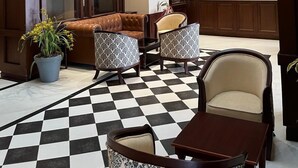 Un vestíbulo con suelo a cuadros, sofás de cuero, sillones estampados y una decoración con cabeza de ciervo.