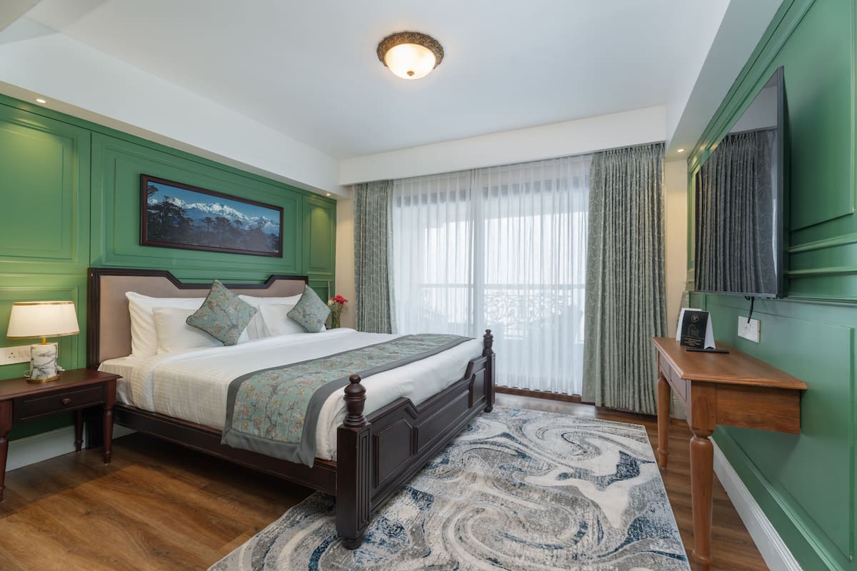 Een slaapkamer met een groot bed, nachtkastje, dressoir, televisie en een raam met gordijnen.