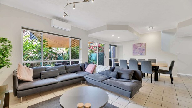 A modern living room with a sectional sofa, a round coffee table, and a dining area with chairs and a table. - Tranquil 3-Bed Unit with Lush Garden Views (Taringa)