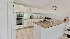 A modern kitchen with white cabinets, a built-in oven, a sink, and a clock on the wall. - Tranquil 3-Bed Unit with Lush Garden Views (Taringa)