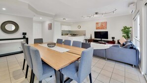 A modern living room with a dining area, a sofa, a TV, and a kitchen in the background. - Tranquil 3-Bed Unit with Lush Garden Views (Taringa)