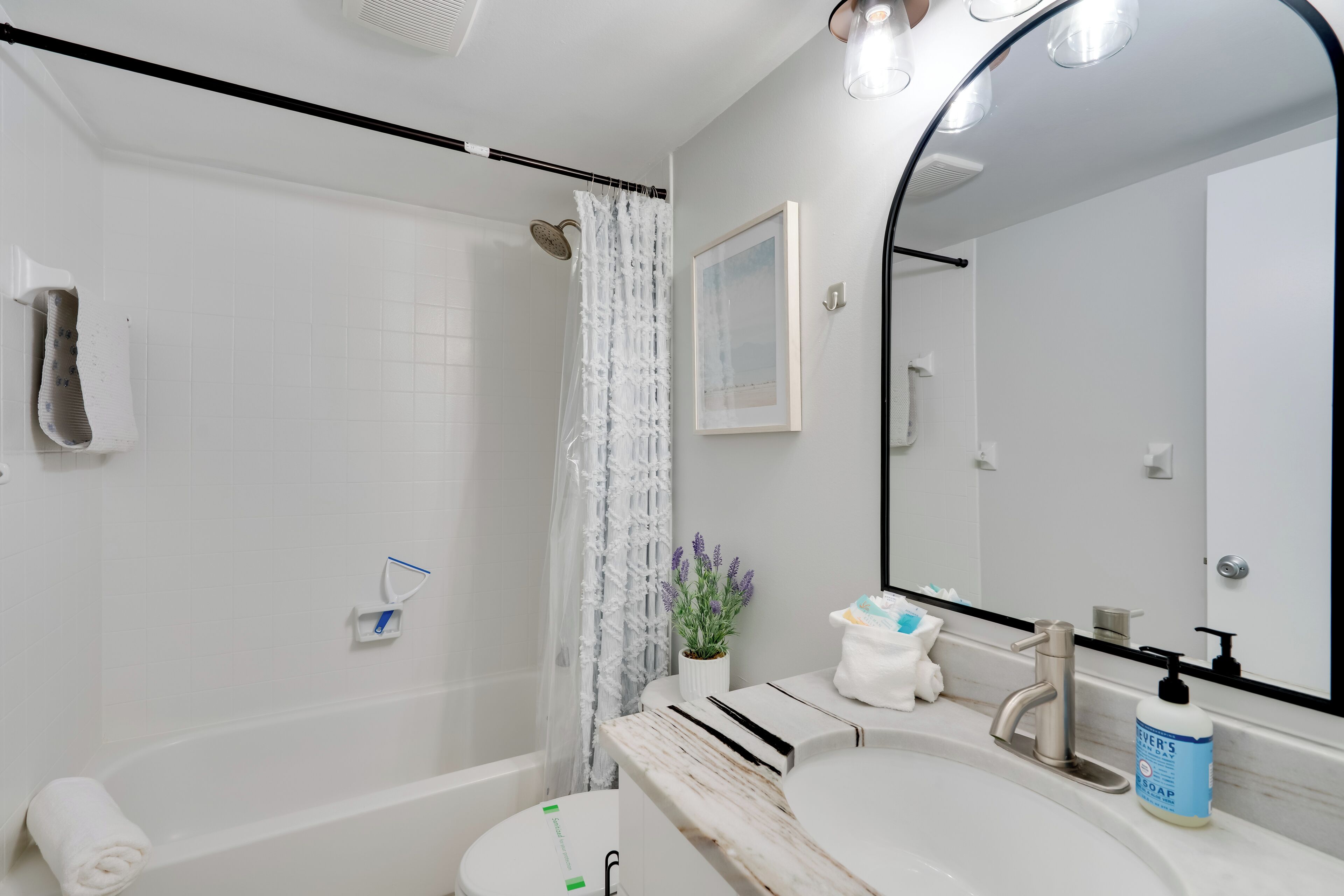 A modern bathroom with a bathtub, a shower with a curtain, a sink with a mirror, and a soap dispenser.