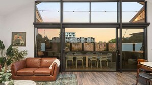 Ein modernes Wohnzimmer mit einer großen Glaswand, einem braunen Ledersofa, einem Essbereich mit Stühlen und einem kleinen Tisch.