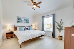 Ein Schlafzimmer mit einem hölzernen Bett, zwei Nachttischen, einem Deckenventilator, einem Fenster mit Vorhängen und einem Bild an der Wand.