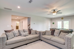 A modern living room with a sectional sofa, a pool table, and a ceiling fan.