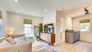 A modern living room with a sofa, a coffee table, and a TV. There is a kitchen area with cabinets and a sink.