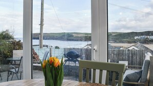 A conservatory with a view of the sea, a wooden table with a vase of tulips, and a chair.